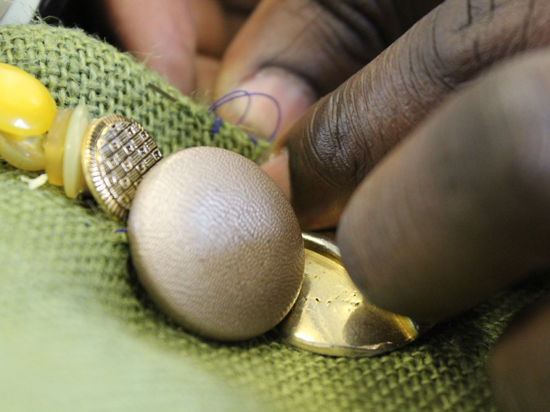 A close up of Andrew's hands sewing a variety of gold buttons on green fabric