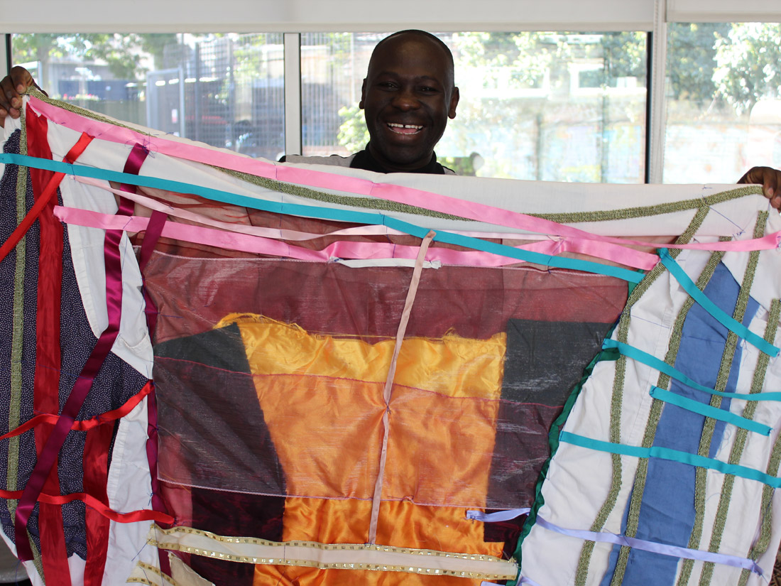 Andrew proudly smiling holding up brightly coloured textile flag he has created