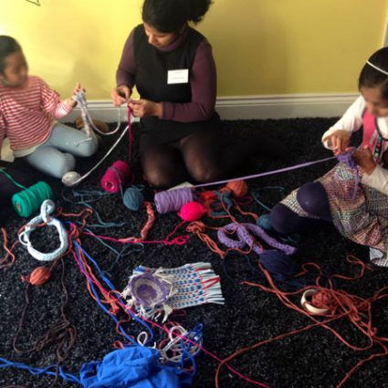 2 Girls sit on the floor with spools of wool scattered around them.