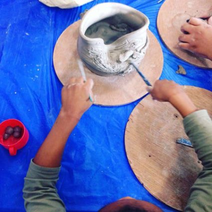5 A young baby pokes a wet clay pot with a paintbrush.