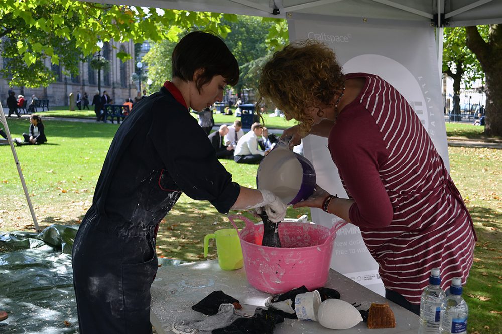 The artist helps a woman pour liquid plaster out of a bowl and into some fabric.