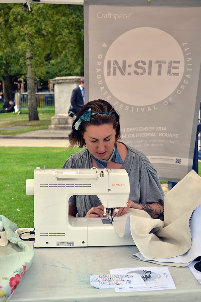 A girl sits at a sewing machine outside in a park.
