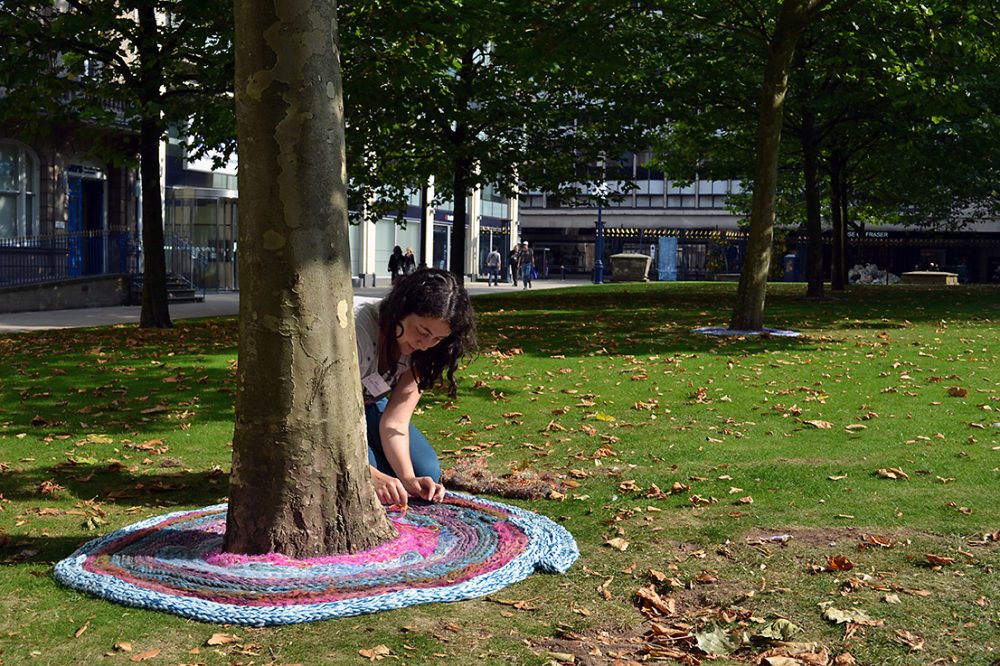 The artist lies the plaited yarn around the tree.