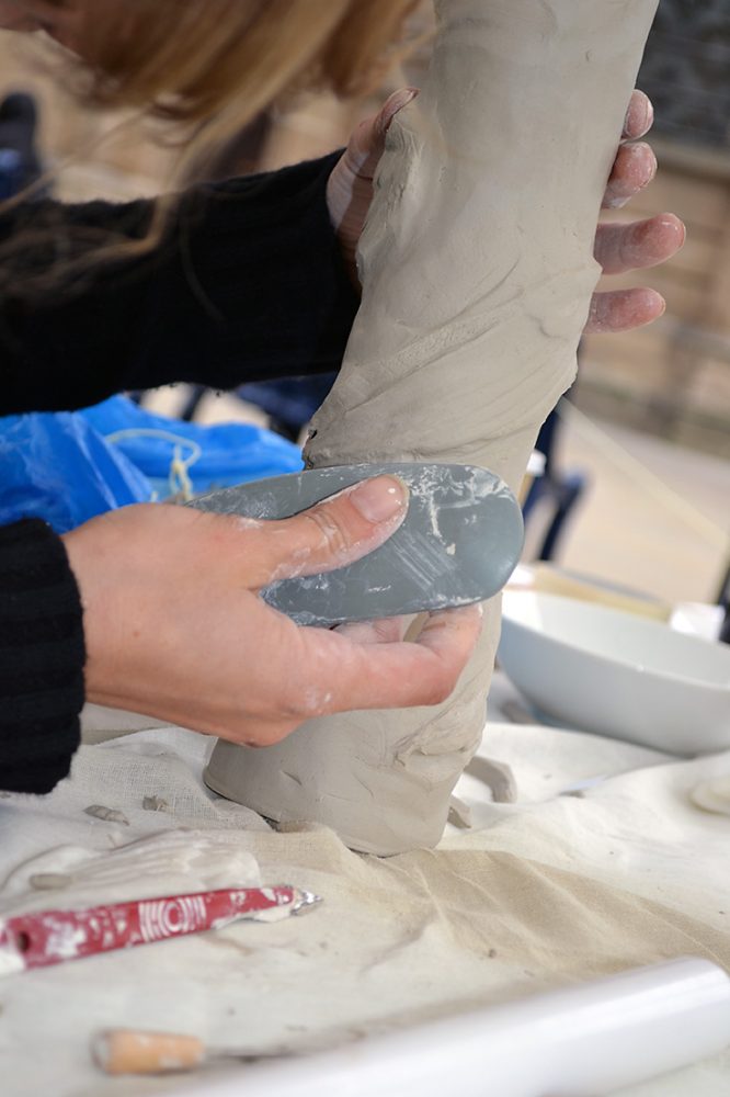The artist uses a rubber kidney to smooth the edges of the clay.