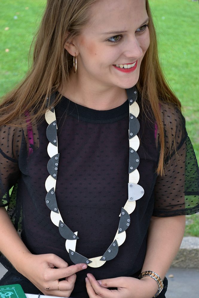 A woman with a long black and white necklace, made of semi circles and bolted together, around her neck smiles.