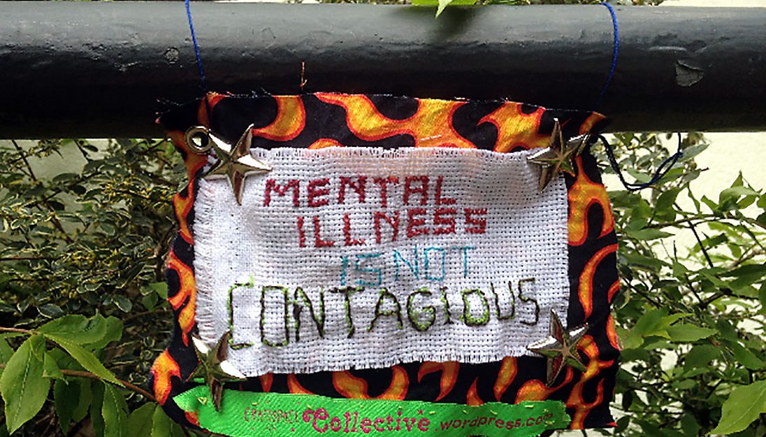 Sign made out of different fabrics with a stitched message about mental health and metal stars.