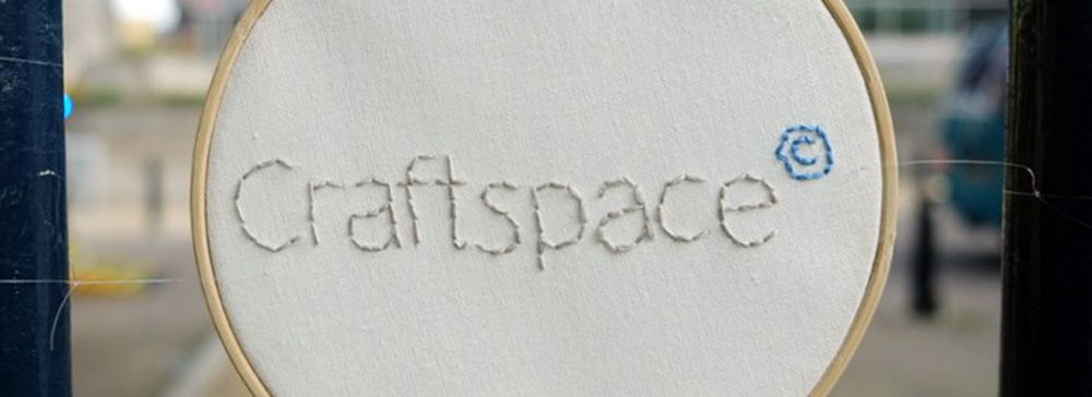 The Craftspace logo stitched into white cloth on an embroidery hoop.