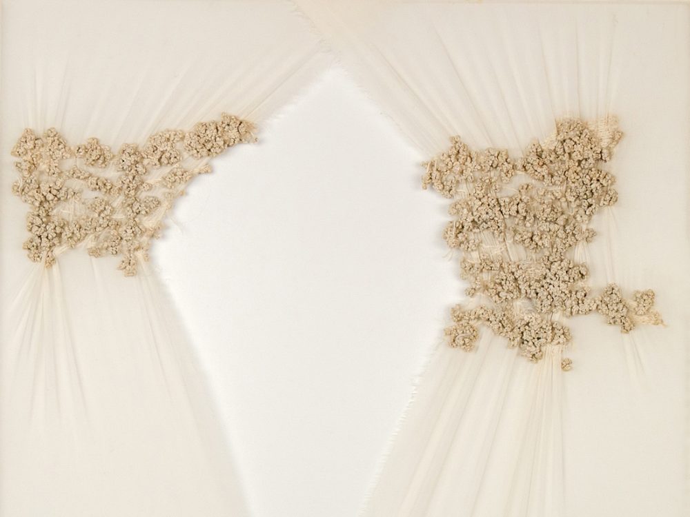 Sheets of cream material delicately draped, with cream coloured thread embroidered on to the surface.
