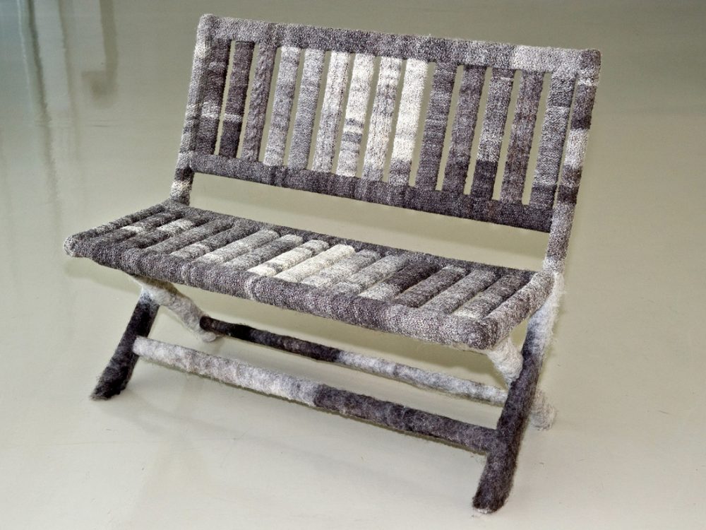 A bench covered in hand knitted grey and white woollen pieces.