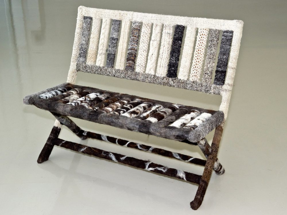 A bench covered in patterned woollen pieces of various cream, grey and brown colours.
