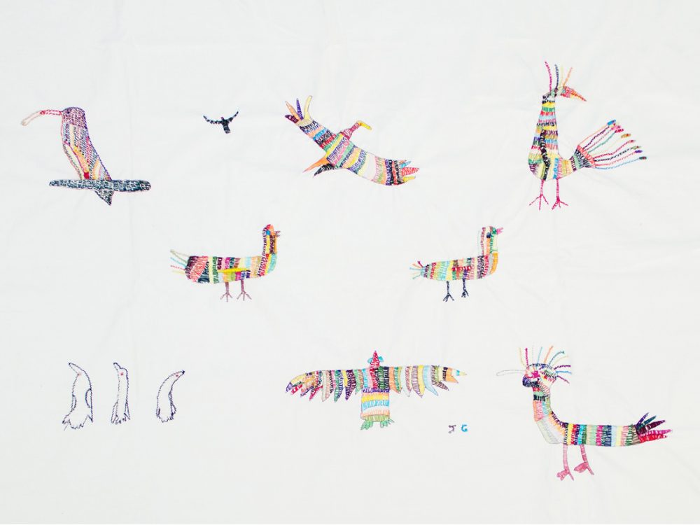 a white sheet is embroidered with small colourful birds. the style is quite naive.