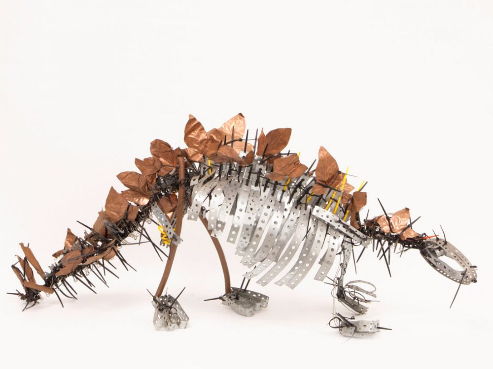 A dinosaur figurine made from found materials, off cuts and scraps of metal and plastic.