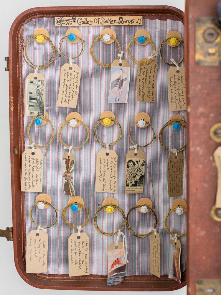 Inside of the case showing broken strings resting on hooks with brown tags attached to them.