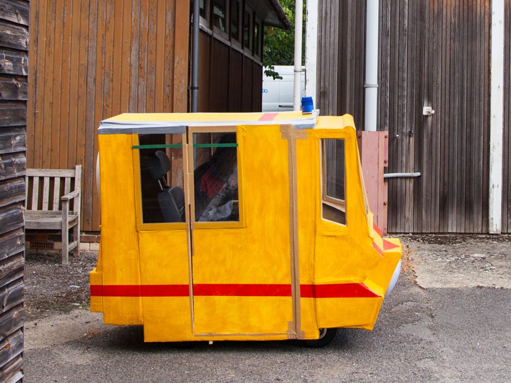 A small vehicle is crudely made from cardboard and painted bright orange.