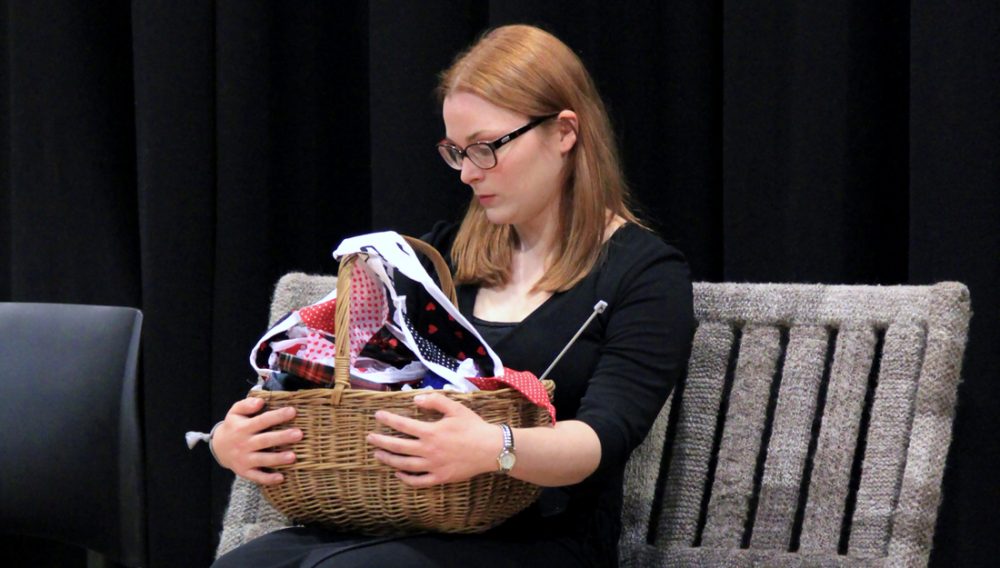 A woman sits on a bench holding a basket filled with wool, knitting needles and bunting.