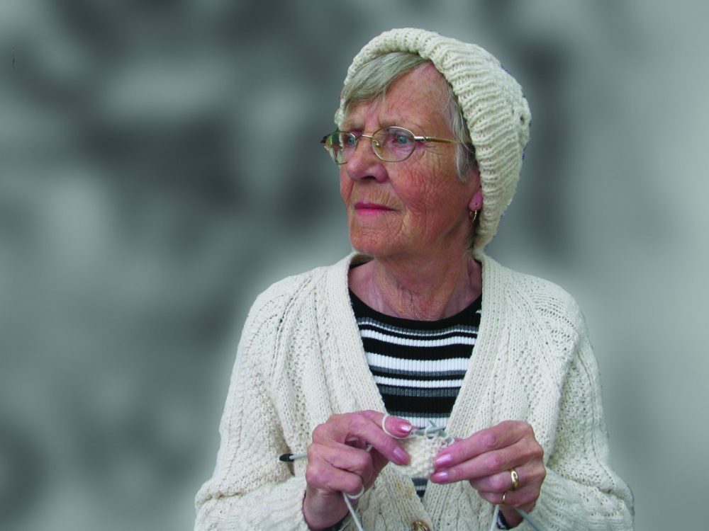 older lady wearing knitted hat and cardigan is knitting