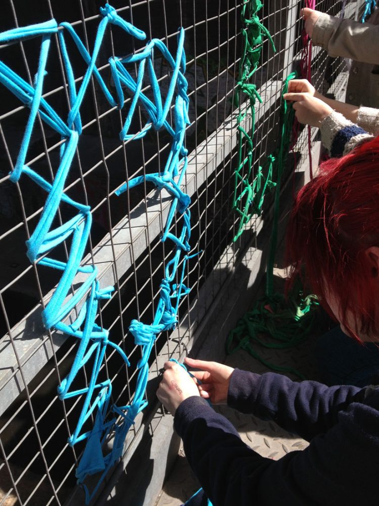 A woman weaves yarn through a metal gate to create the letter D.