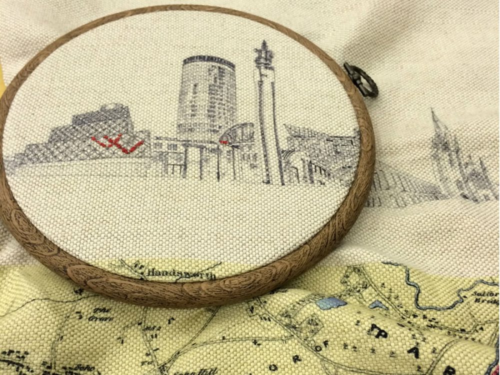 embroidery hoop with printed design of Birmingham city skyline with some parts sewn in red thread