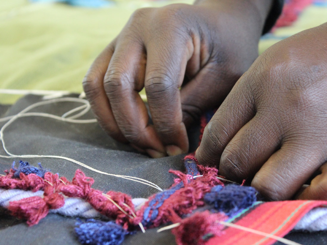 A close up of Andrew's hands carefully sewing different textures onto his textile works