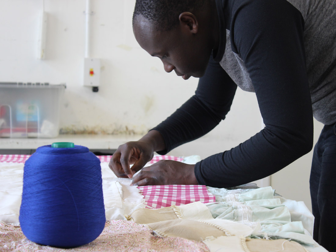 Andrew concentrating sewing with a big spool of bright blue thread next to him