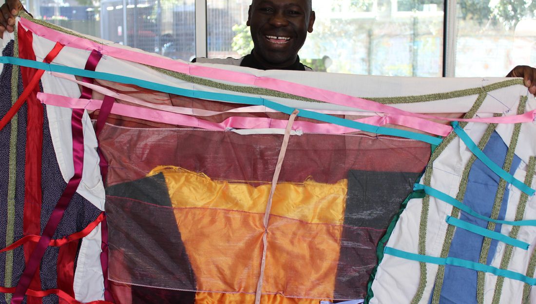 Andrew proudly smiling holding up brightly coloured textile flag he has created