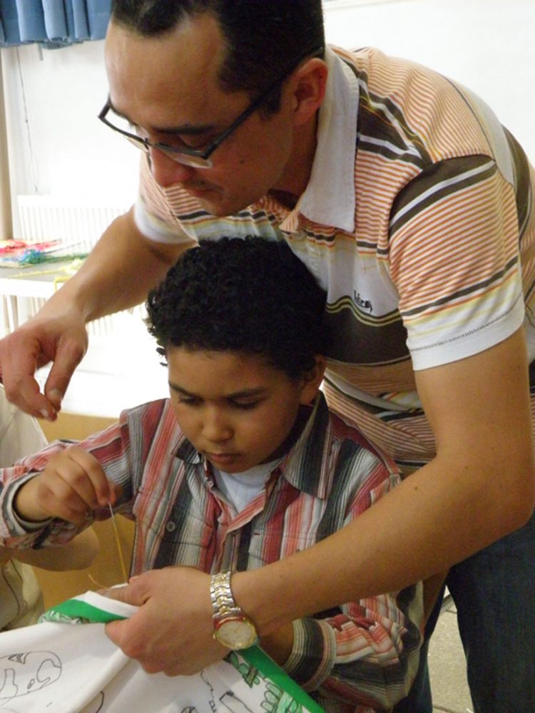A man helps a child sew into fabric.