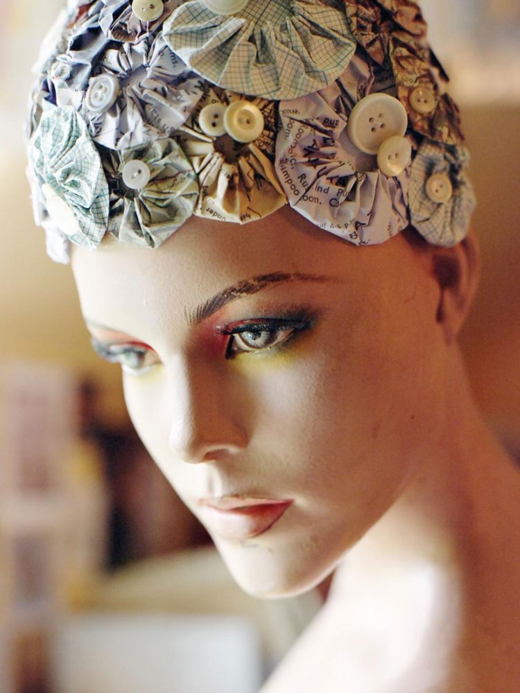 A mannequin with a bath hat on its head made from intricately folded paper and buttons.