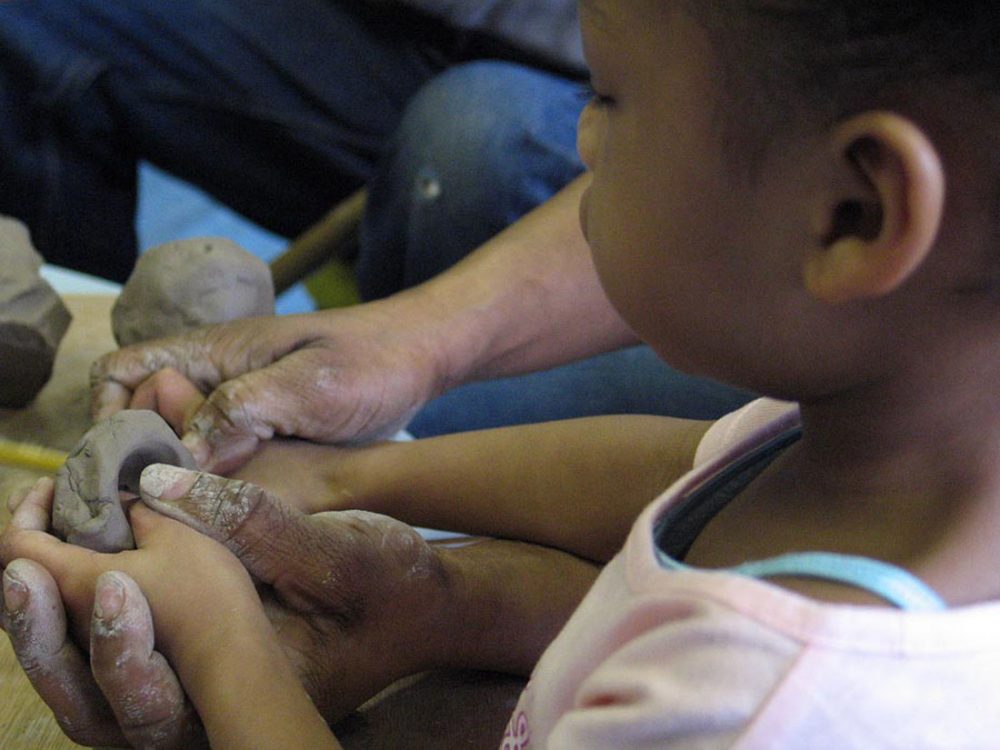 A young boy pushes his thumb into wet clay.
