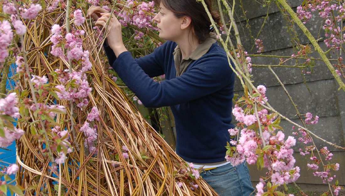 An artist weaves flowers into a willow sculpture.