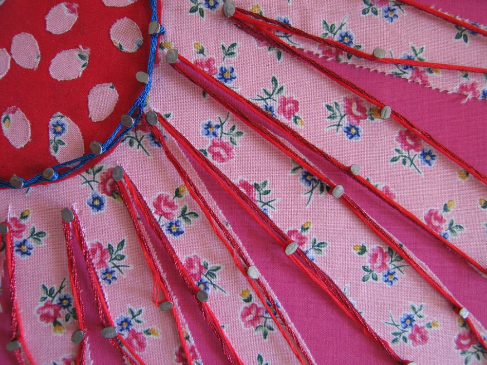 A close up detail of pins on floral brightly coloured fabric with thread woven around them.