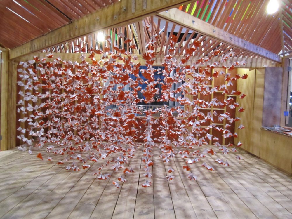 Lots of geometric shapes made from orange and white origami paper hang from the ceiling in a room.
