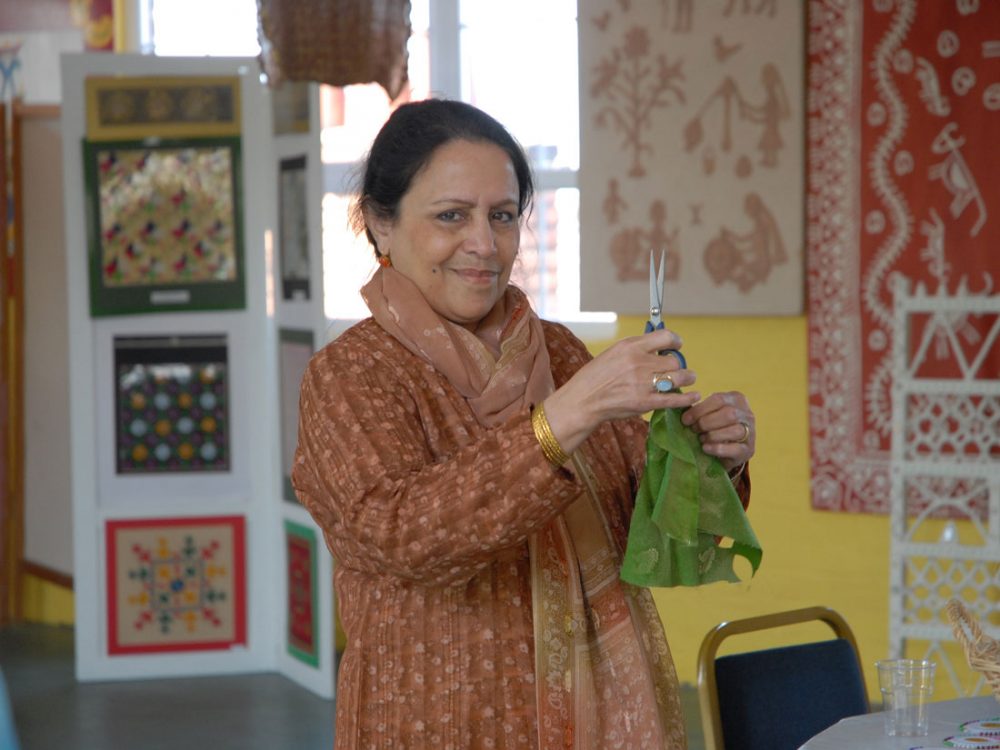 A woman holds a pair of scissors and a green piece of fabric whilst smiling at the camera.