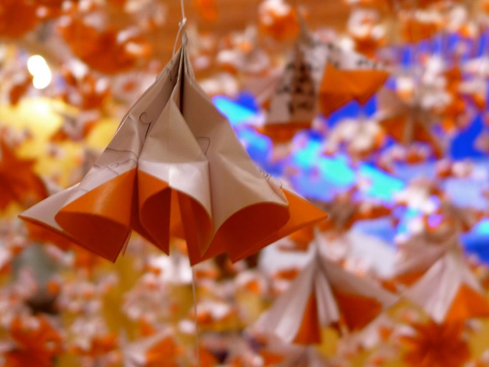 A geometric shape made from origami paper hangs from the ceiling using string, with more in the background.