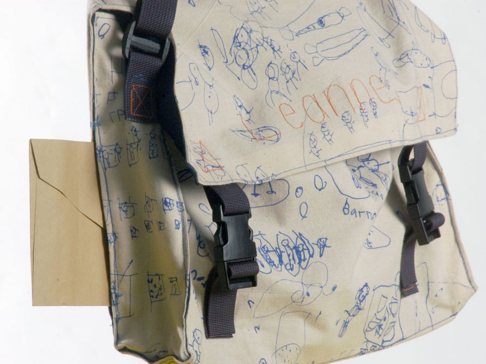 A close up of a white bag with various drawings and writing from children printed on to it.