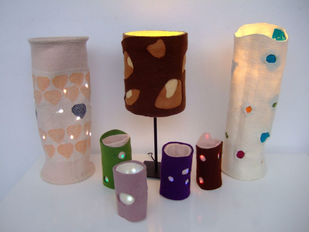 Seven light shades made out of felt of various colours with holes cut into them.