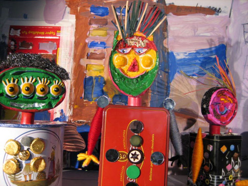 Three brightly painted figures made from found objects including tin boxes.