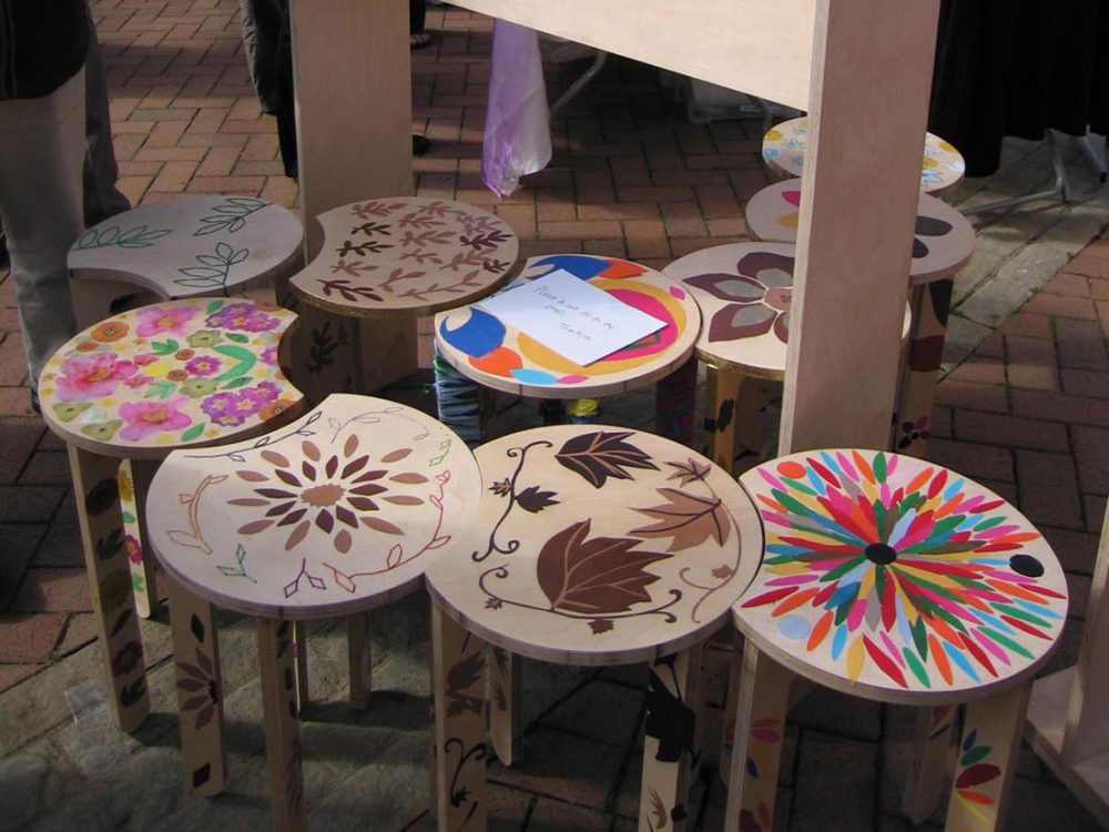 Ten stools sit next to one another with various nature themed designs stuck and stitched on to them.