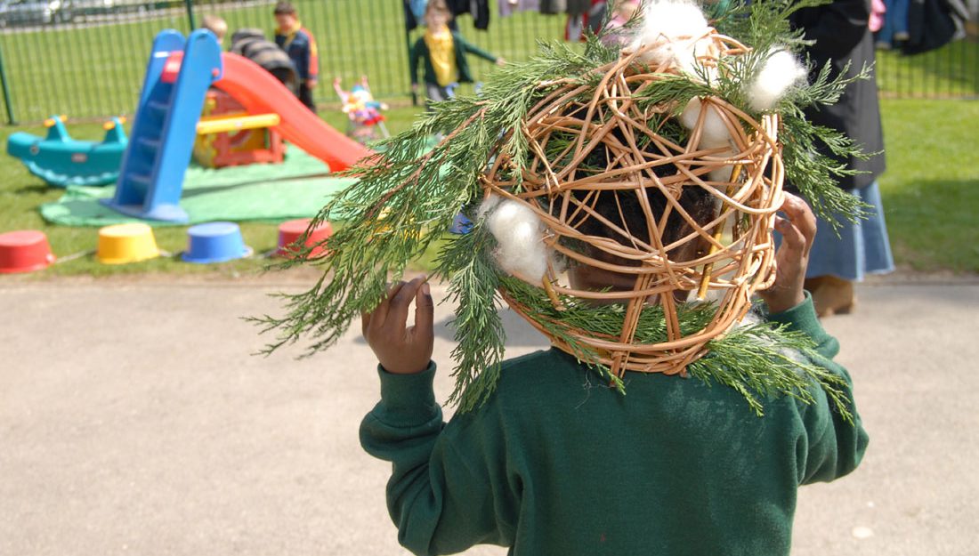 A young child places a small woven willow sculpture onto his head.