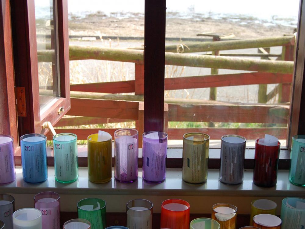 Tall glass beakers of various colours and opacities sit on a window sill with paper inside of them.