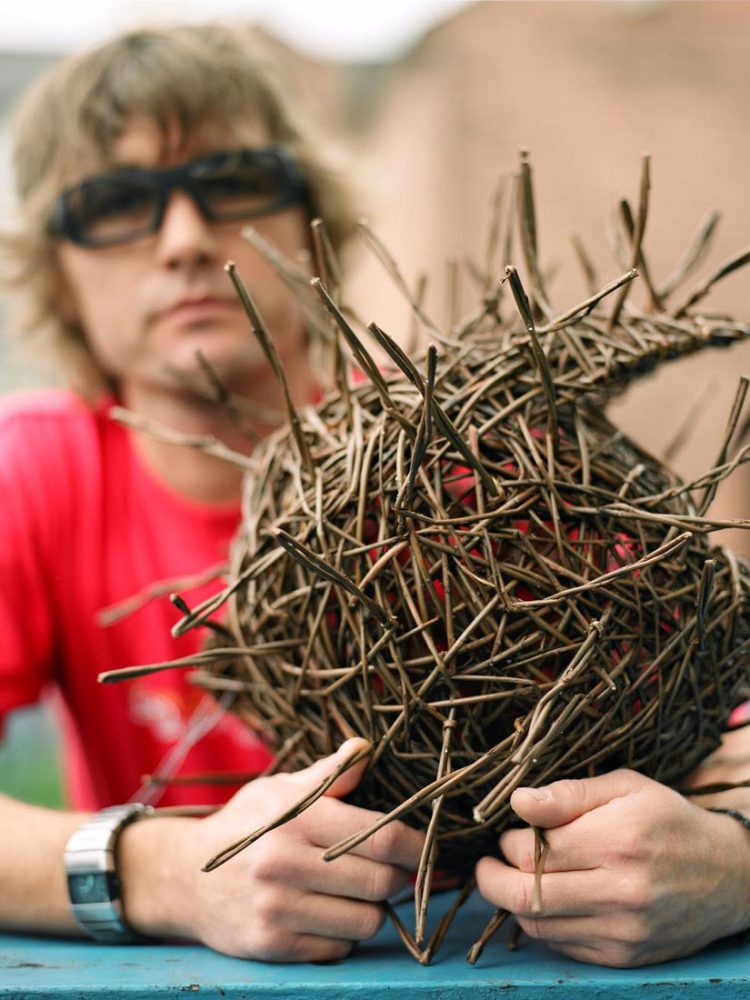 The artist holds a small sphere shaped intricate willow sculpture.