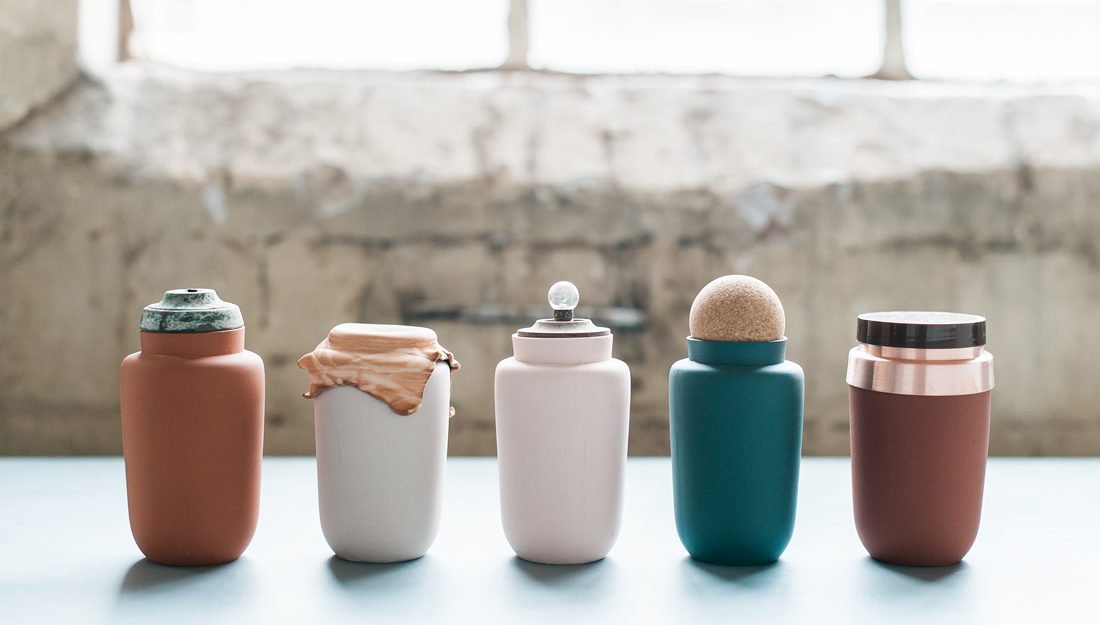 A row of simple shaped ceramic vessels with additions of found objects such as lids and cloth covers.