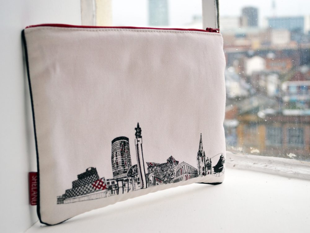 The i pad case sits on a windowsill. They are simple in design with a black and white line drawing of the skyline and red trimmings.