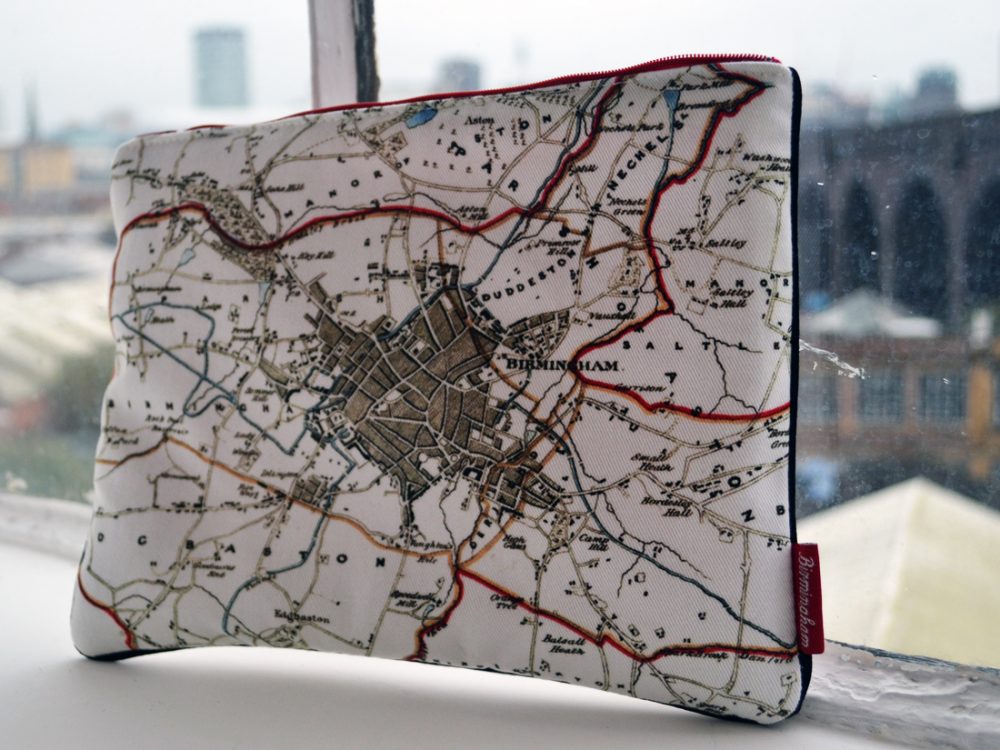 The i pad case sits on a windowsill. They are simple in design with a black and white line drawing of the skyline and red trimmings.