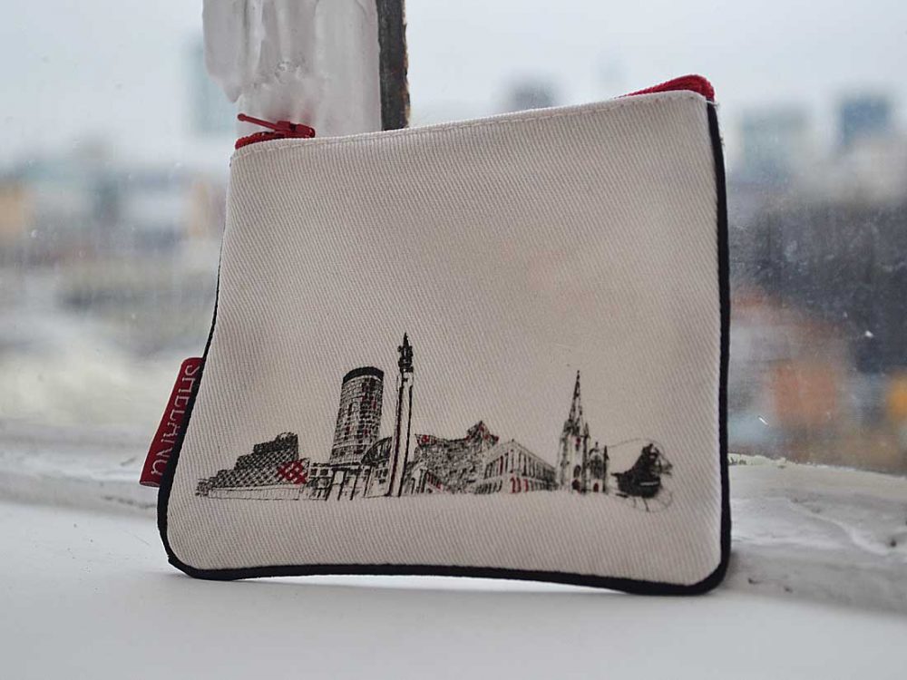 The purse sits on a windowsill. It is simple in design with an old map of birmingham printed onto it and red trimmings.The tag says 'birmingham'.