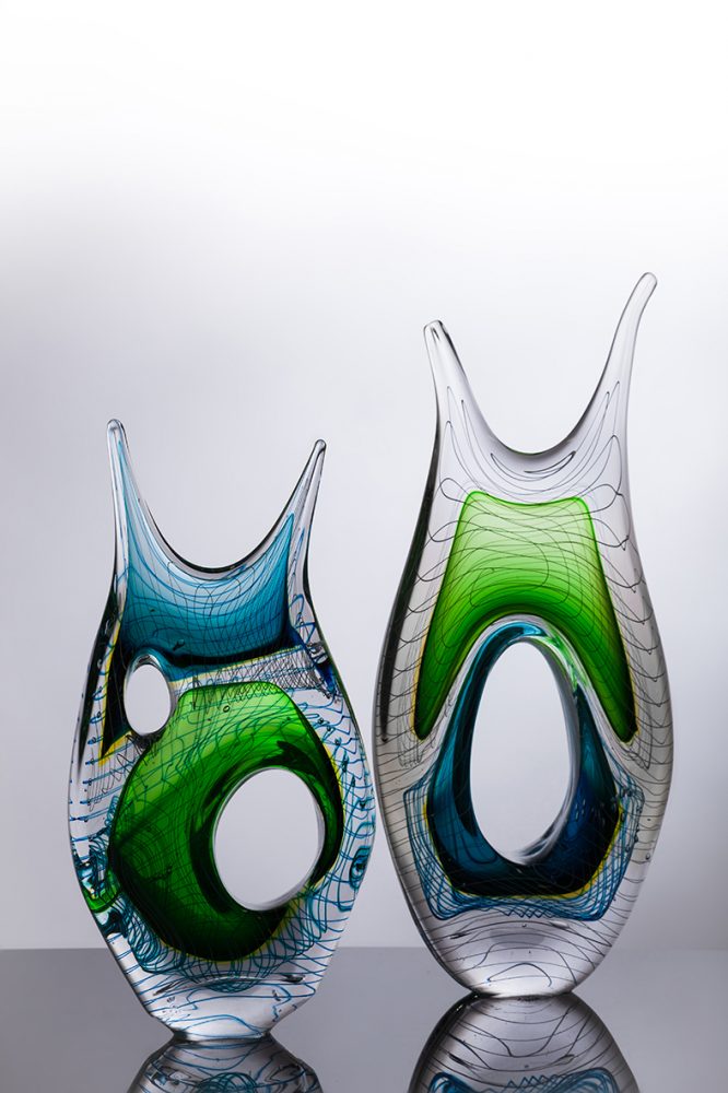 2 glass sculptures: they are organic shaped with bright sections and a linear pattern.