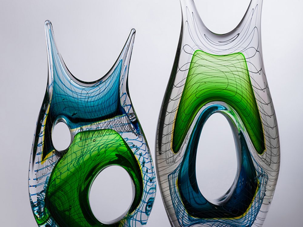 2 glass sculptures: they are organic shaped with bright sections and a linear pattern.