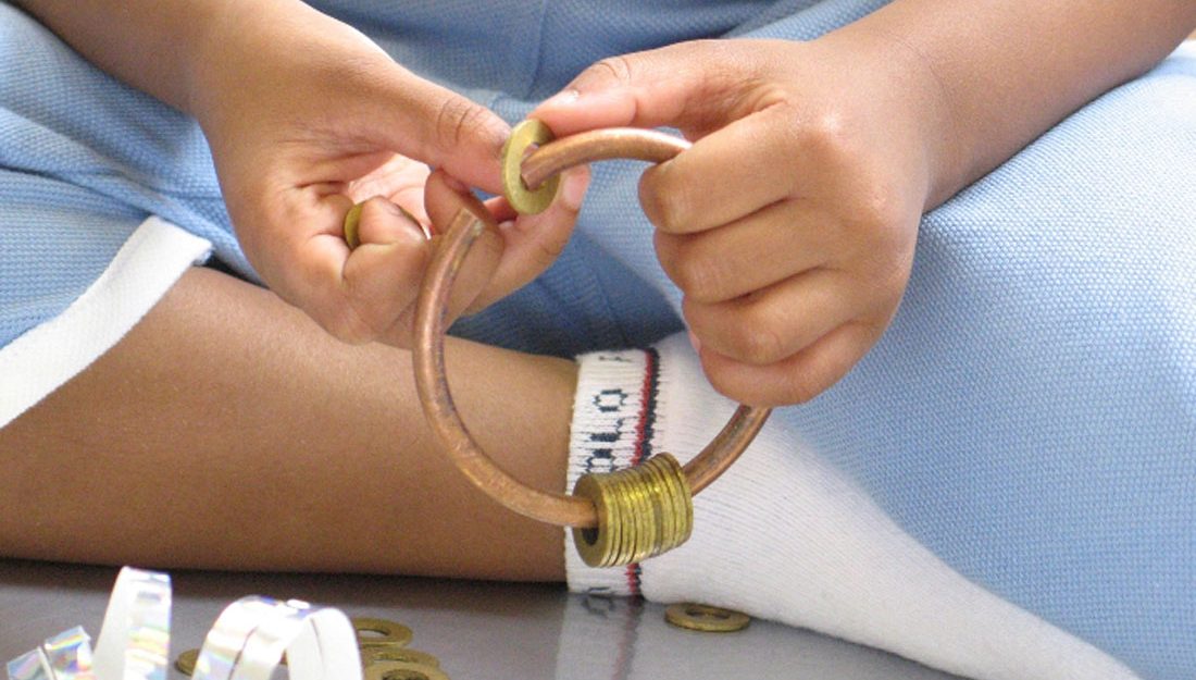 A child puts metal washers on to a copper hoop.