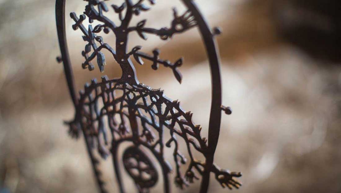A section of a detailed piece of ironwork. A cut out design shows shapes like hands and tree forms.