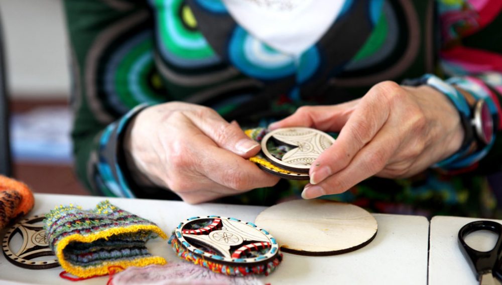 A pair of hands intricately embroider around and inside a wooden disc.