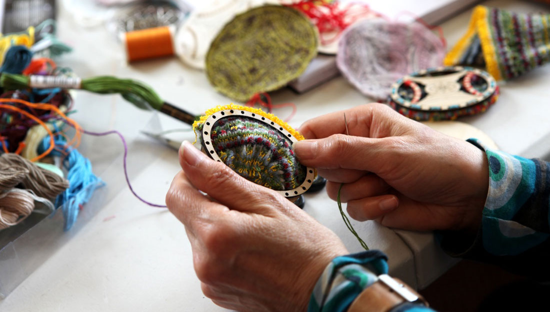 A pair of hands intricately embroider around and inside a wooden hoop.